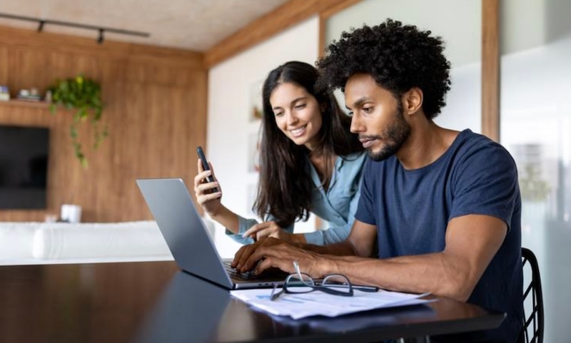 Joven pareja usando una computadora portátil y un teléfono inteligente en casa