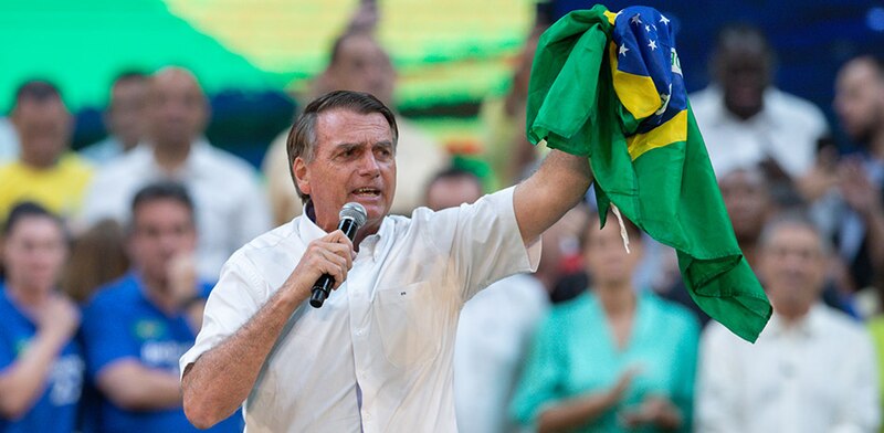 El presidente Jair Bolsonaro sostiene una bandera brasileña durante un discurso.