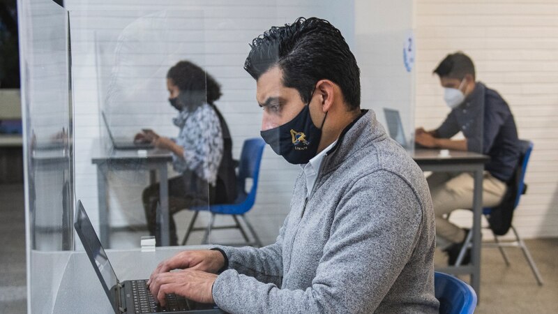 Estudiantes universitarios con mascarillas trabajando en sus ordenadores portátiles
