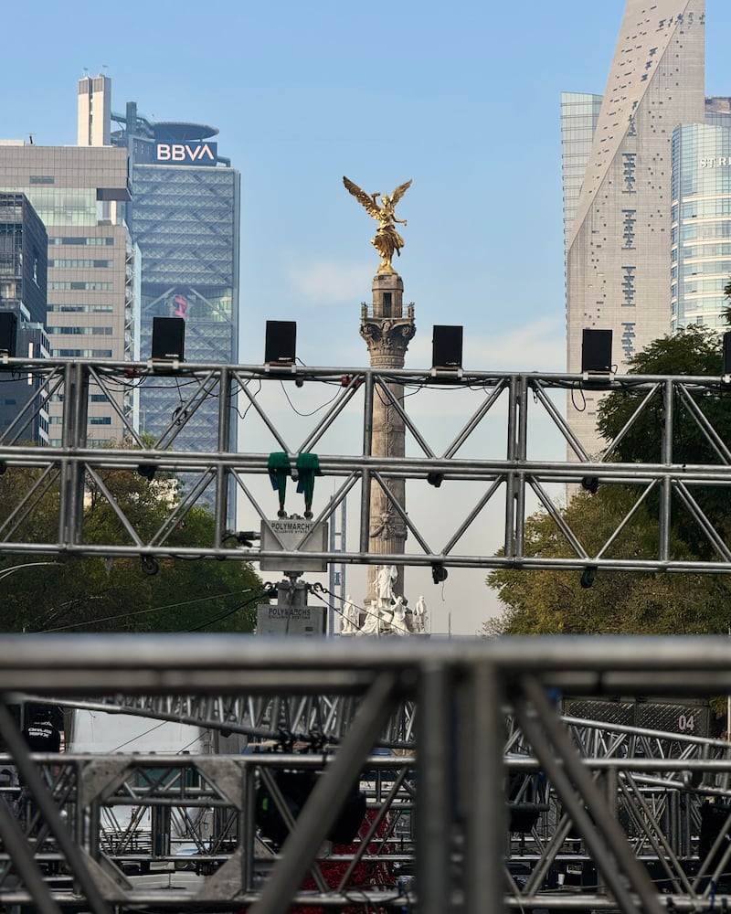 na vista en perspectiva del Monumento a la Independencia (Ángel de la Independencia) en la Ciudad de México, enmarcada por estructuras metálicas de audio e iluminación (equipo Polymarchs) instaladas para un evento público. Al fondo se aprecian la Torre BBVA y la Torre Reforma.