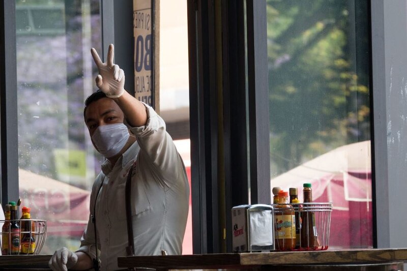 Camarero con mascarilla y guantes haciendo el signo de la paz