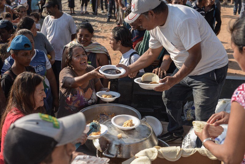 Un grupo de personas reciben comida de una olla grande en una situación de pobreza y necesidad.