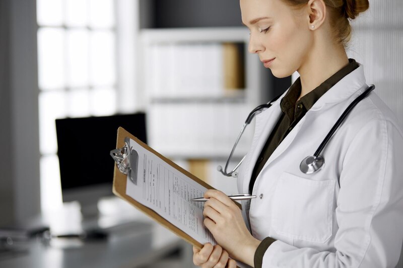 Doctora en bata blanca escribiendo en un portapapeles