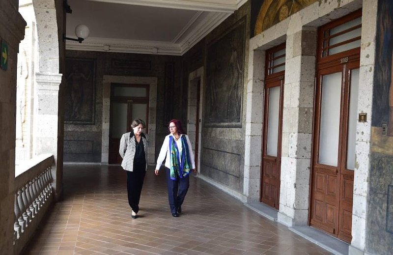 Dos mujeres caminan por un pasillo con arcos y pinturas en las paredes.