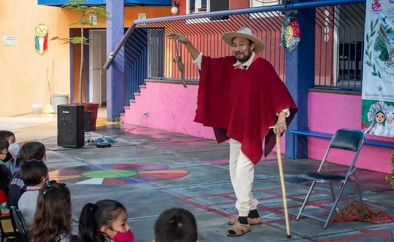 Un hombre con un sombrero y una capa roja sostiene una rata en su mano y la muestra a un grupo de niños que lo miran atentos.