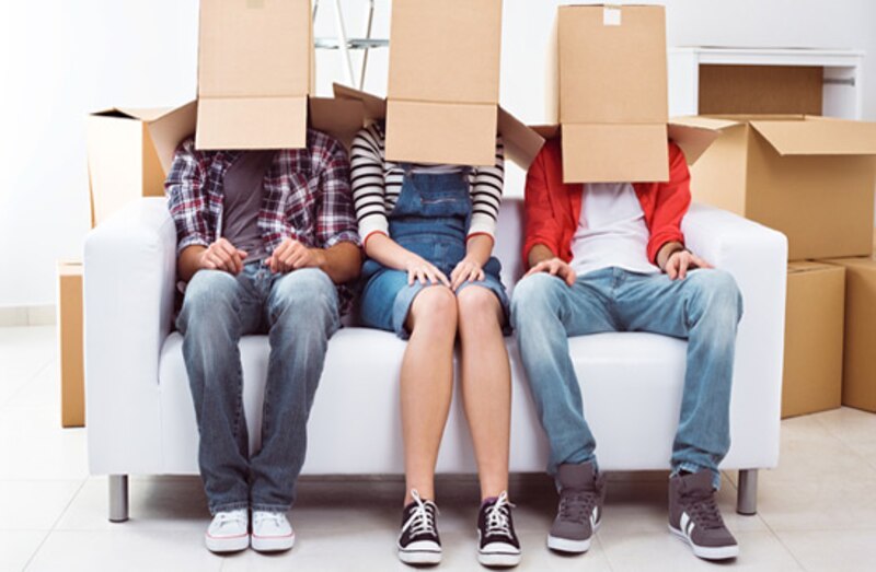 Tres personas con cajas de cartón en la cabeza están sentadas en un sofá