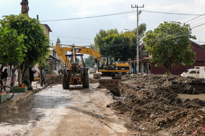 Maquinaria pesada trabajando en una zanja en una calle de tierra.