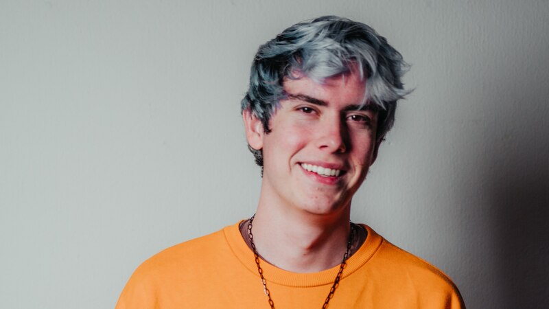 Un joven con el pelo azul sonríe a la cámara.