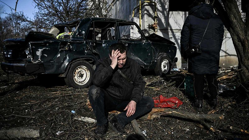 Un hombre se sienta en el suelo junto a un coche destrozado tras un ataque con misiles en Kiev, Ucrania.