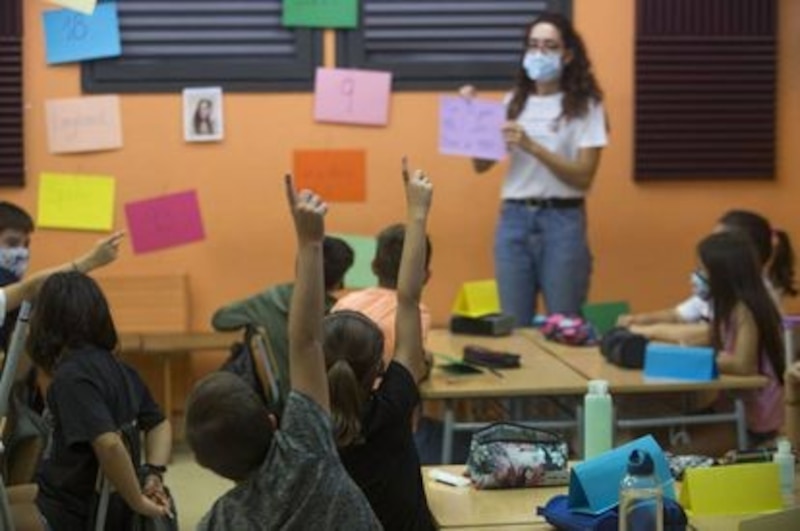 Niños en el aula levantando la mano para responder a la profesora
