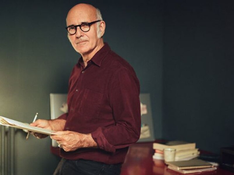 Un hombre mayor con gafas y camisa roja sostiene un libro.