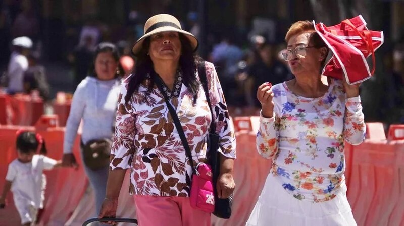 Dos mujeres caminan por una calle en un día caluroso