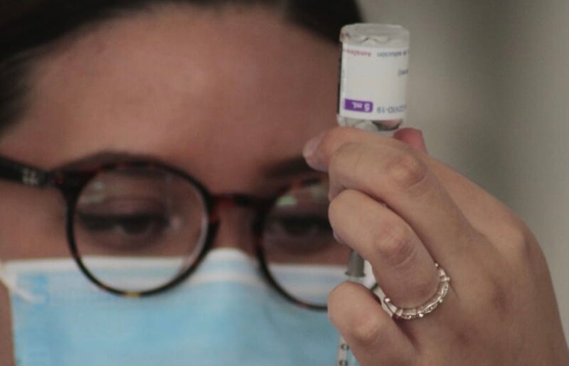 Mujer con mascarilla sosteniendo una jeringa con una vacuna