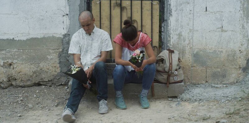 Pareja joven sentada en la acera con flores