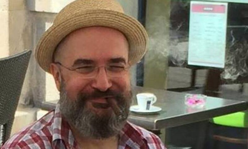 Un hombre con barba y sombrero sonríe mientras fuma un cigarro.