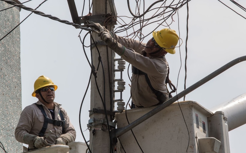 Dos trabajadores de la compañía eléctrica arreglando un cable en lo alto de un poste