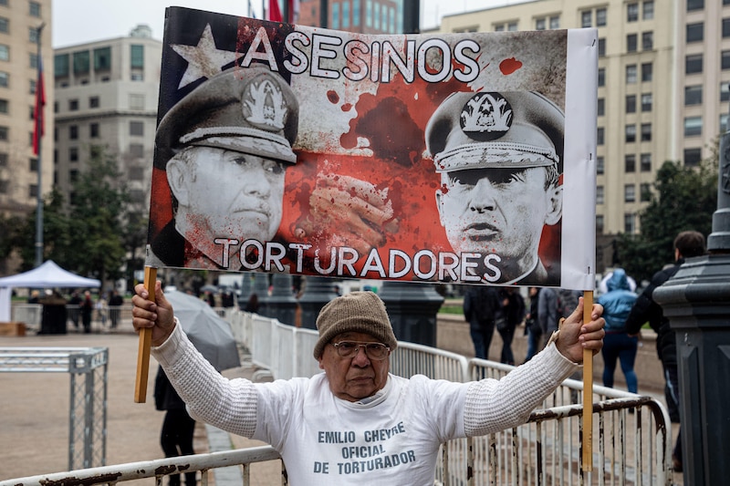 Un hombre sostiene un cartel que dice "Asesinos torturadores"