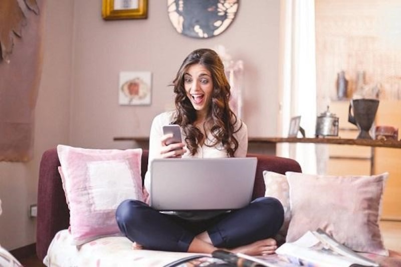 Mujer joven usando su laptop y teléfono en el sofá