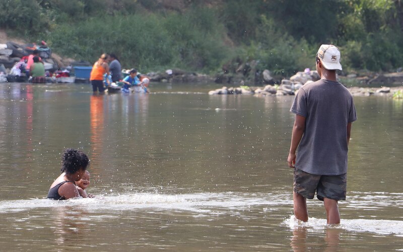 Madre e hijo se bañan en el río mientras el padre observa desde la orilla