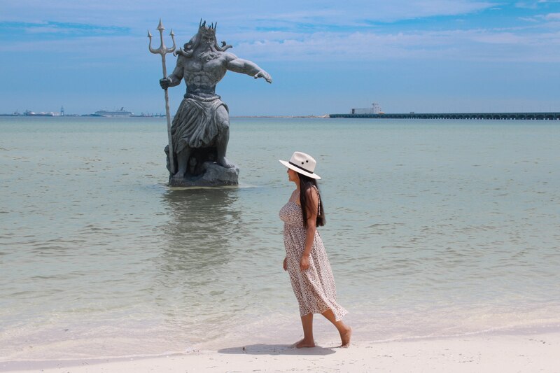 Mujer caminando junto a una estatua de Poseidón en la playa