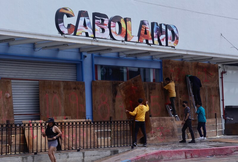 Trabajadores colocando tablones de madera en las ventanas de un negocio