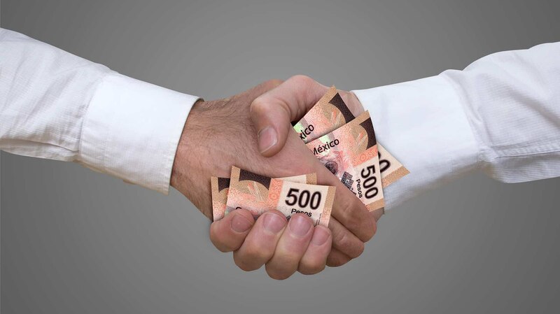 Dos manos estrechándose con billetes de 500 pesos mexicanos.
