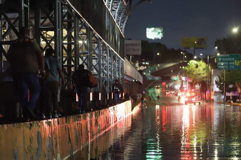 Personas buscan superar la inundación de Circuito Interior pasando por una de las barsas del metro de la Línea 5.