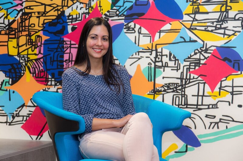 Mujer joven sentada en un sillón azul frente a un mural colorido