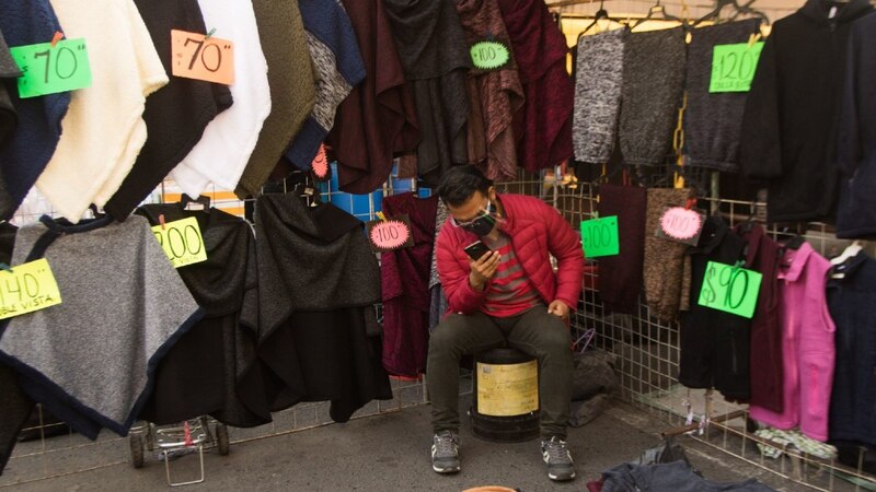 Un hombre mirando su teléfono en un mercado de ropa.