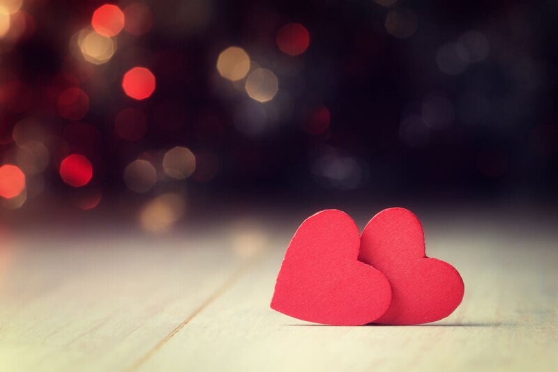 Dos corazones rojos sobre una mesa de madera con un fondo de luces borrosas.