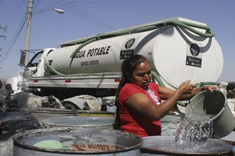 Mujer llenando un balde con agua de un camión cisterna