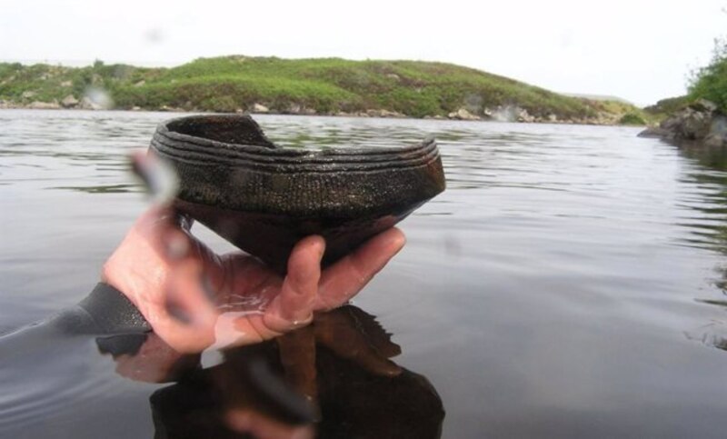Arqueólogo sosteniendo un cuenco de cerámica encontrado en un lago.