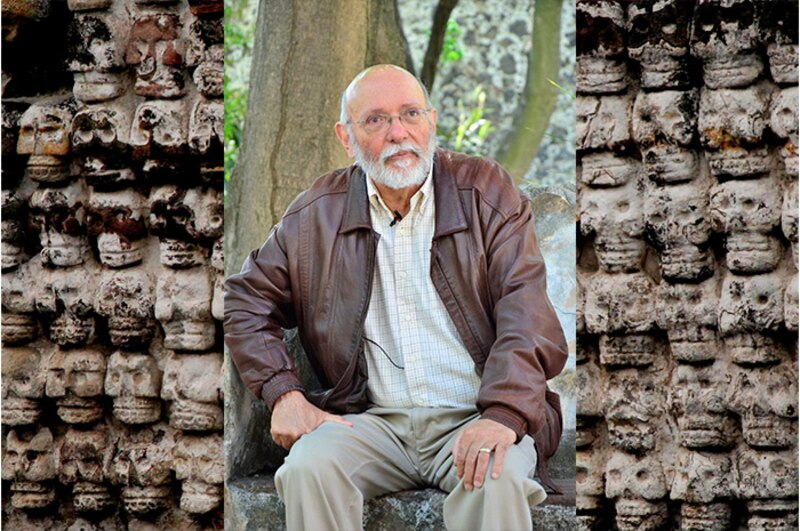 El arqueólogo Eduardo Matos Moctezuma sentado frente a un muro con cráneos tallados