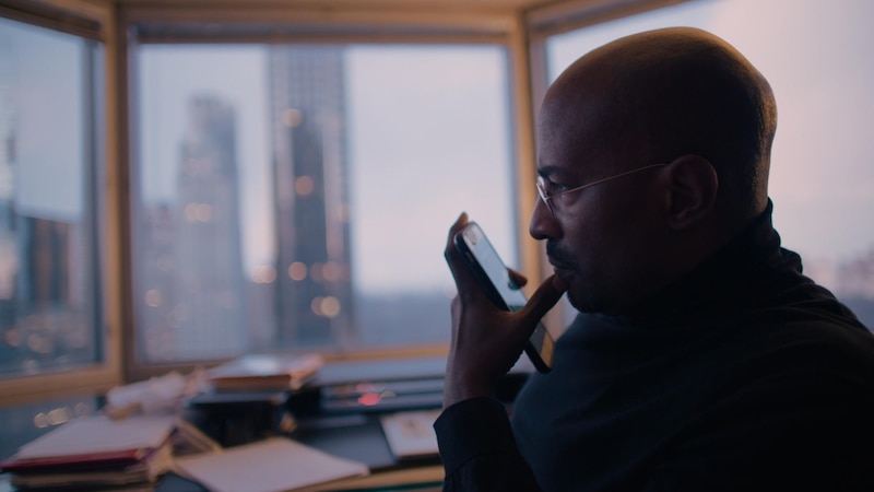 Un hombre negro mirando su teléfono en una oficina con una vista de la ciudad de Nueva York