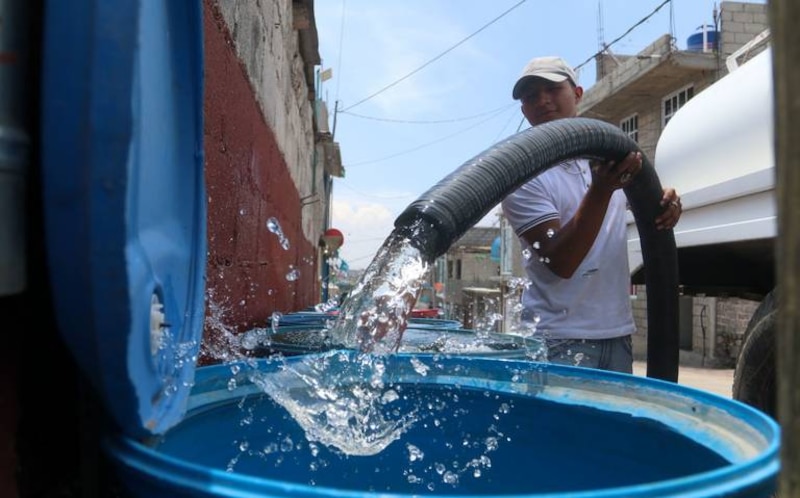 Un hombre llena un recipiente con agua de una manguera