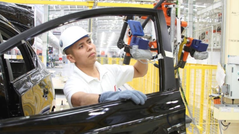 Trabajador de una fábrica automotriz instala una puerta en un automóvil.