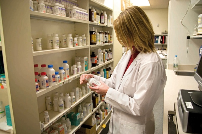 Farmacéutica revisando medicamentos en la estantería de una farmacia