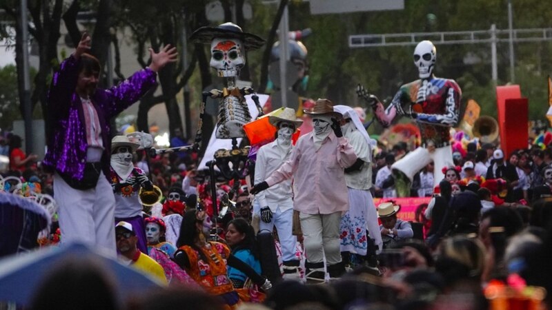 Imagen del desfile del Día de Muertos de la Ciudad de México sobre paseo de la Reforma con figuras de Catrinas y Catrines.