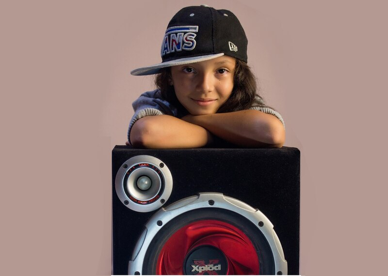 Niña con gorra negra y sudadera gris apoyada en un subwoofer.