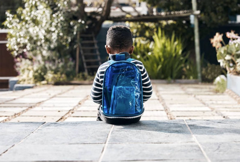 Niño sentado en un escalón con una mochila azul