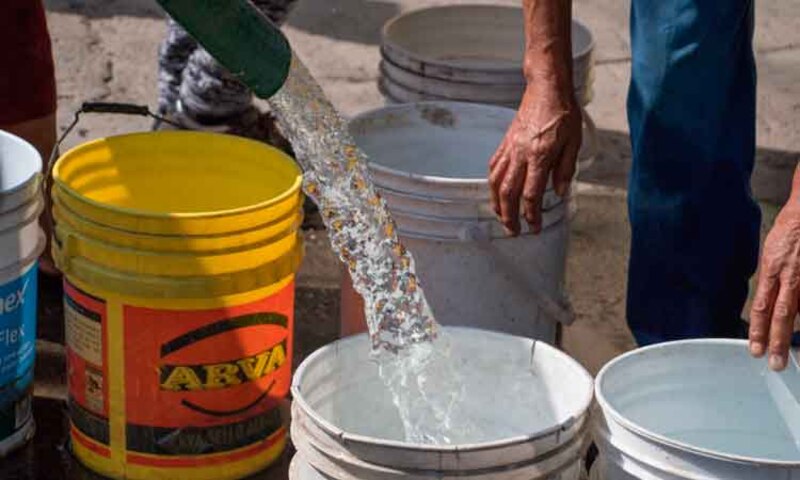 Personas en una comunidad recolectando agua de un grifo público.