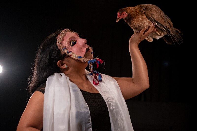 Mujer con máscara sosteniendo un pollo