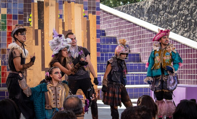 Actores vestidos con trajes extravagantes representan una obra de teatro al aire libre.