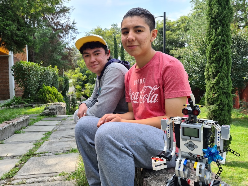 Dos adolescentes sonríen junto a un robot que han construido.