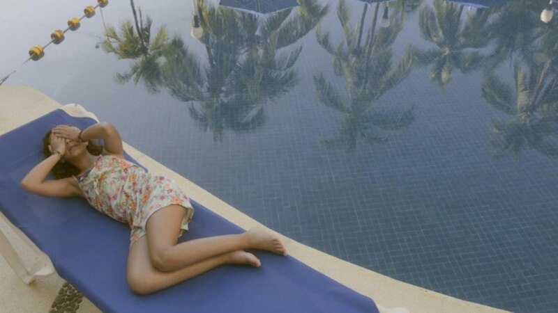 Niña tomando el sol en una tumbona junto a la piscina