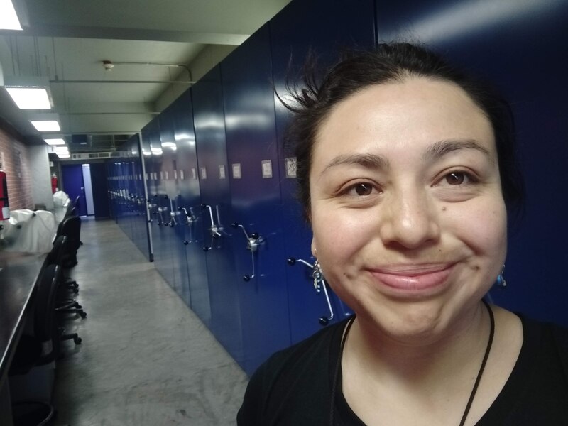 Una mujer sonríe en un pasillo de estanterías azules.