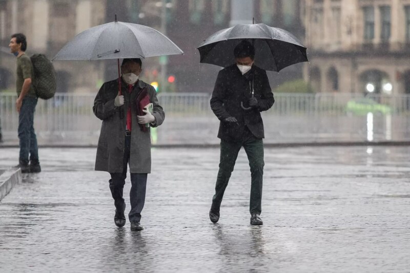 Dos hombres caminan bajo la lluvia con paraguas en la Ciudad de México.