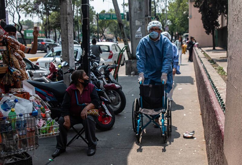 Un médico en silla de ruedas pasa junto a una mujer sentada en la calle