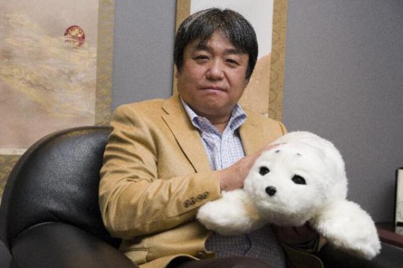Un hombre sostiene un robot con forma de foca en sus brazos.