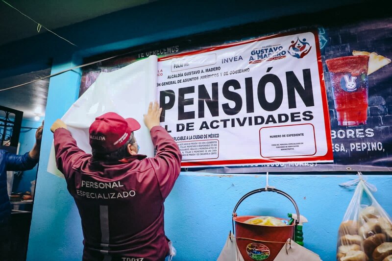 Un hombre coloca un cartel de "Pensión de Actividades" en una pared.